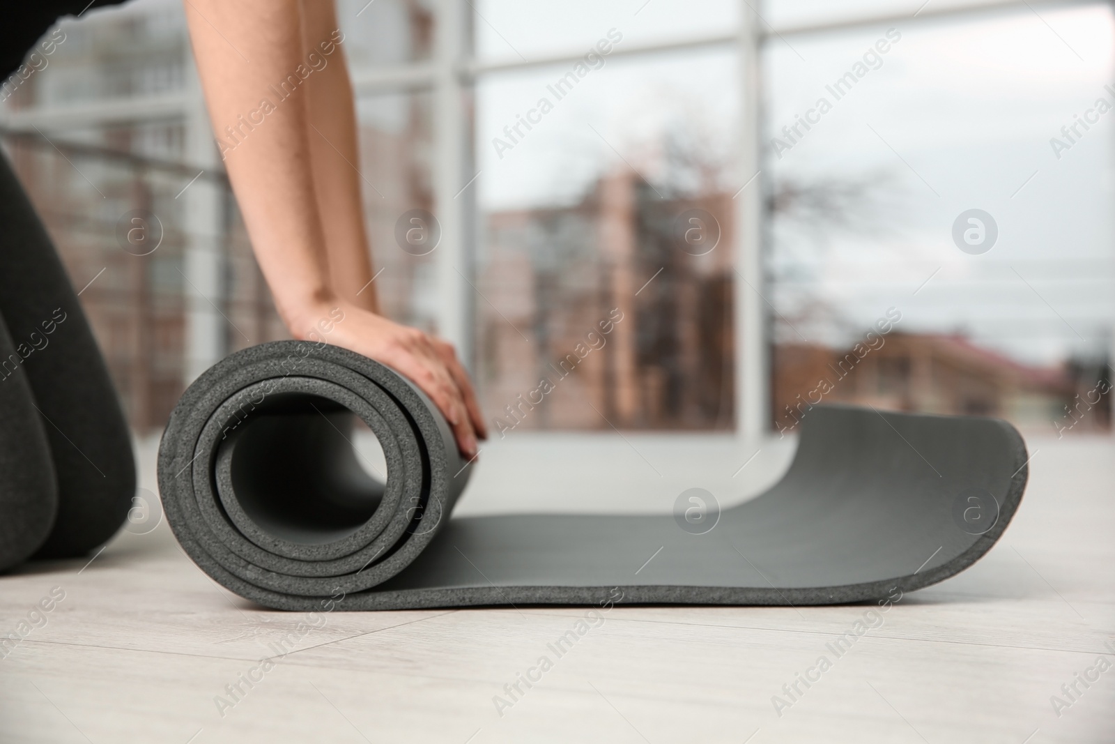 Photo of Woman rolling yoga mat on floor indoors, closeup. Space for text