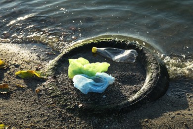 Photo of Plastic trash and tire on sand near water. Environment pollution