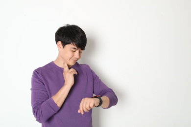 Young man checking pulse on light background