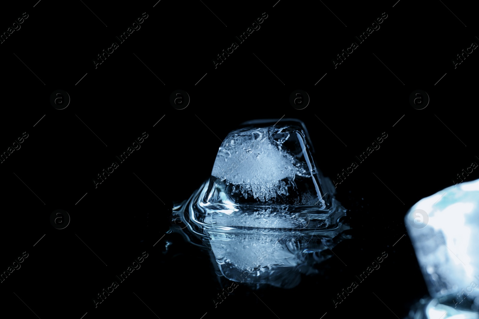 Photo of Transparent ice cube on black mirror surface. Space for text