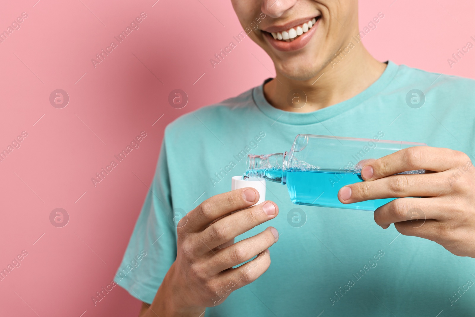 Photo of Young man using mouthwash on pink background, closeup