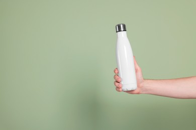 Photo of Man holding thermo bottle with drink on olive background, closeup. Space for text