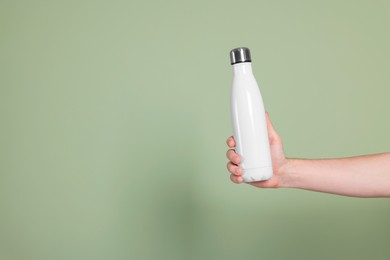 Man holding thermo bottle with drink on olive background, closeup. Space for text