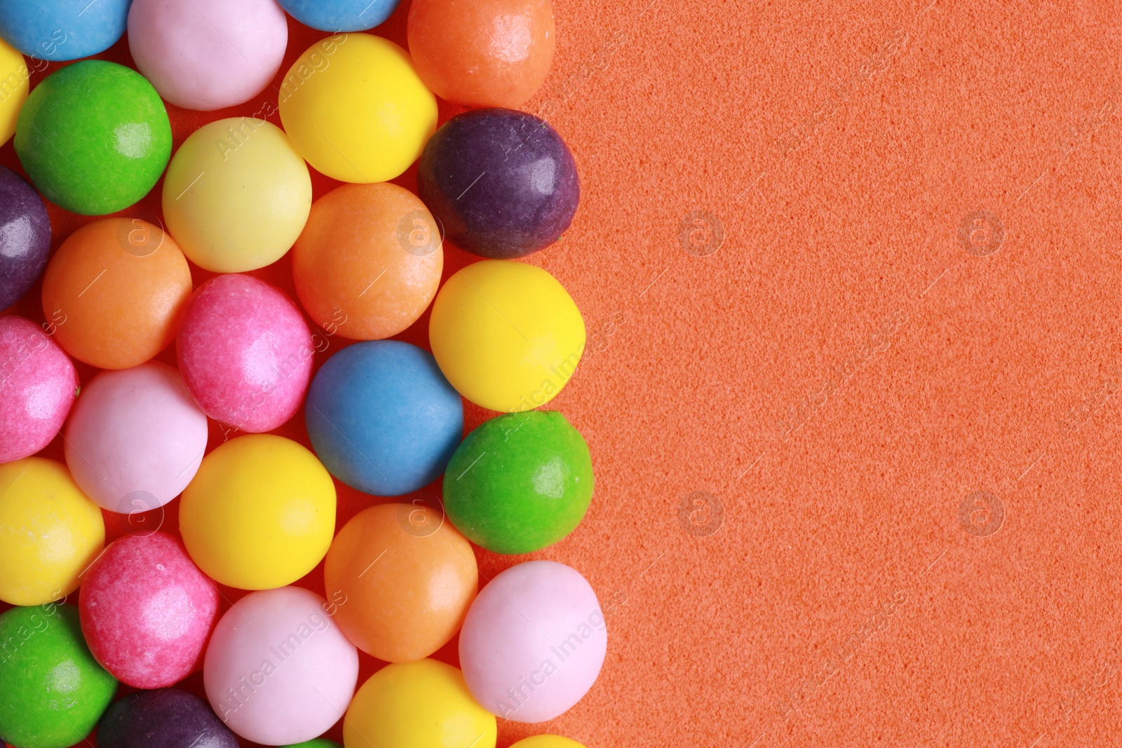 Photo of Many delicious colorful dragee candies on coral background, flat lay