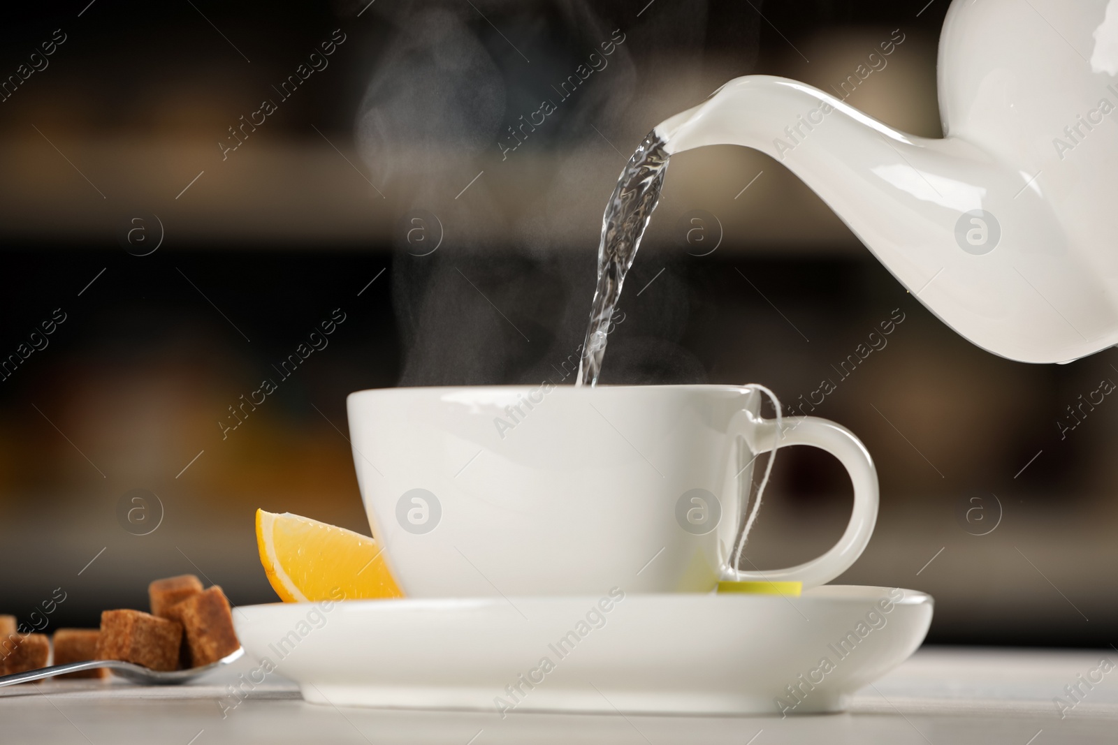 Photo of Pouring hot water into cup with tea bag at white table against blurred background