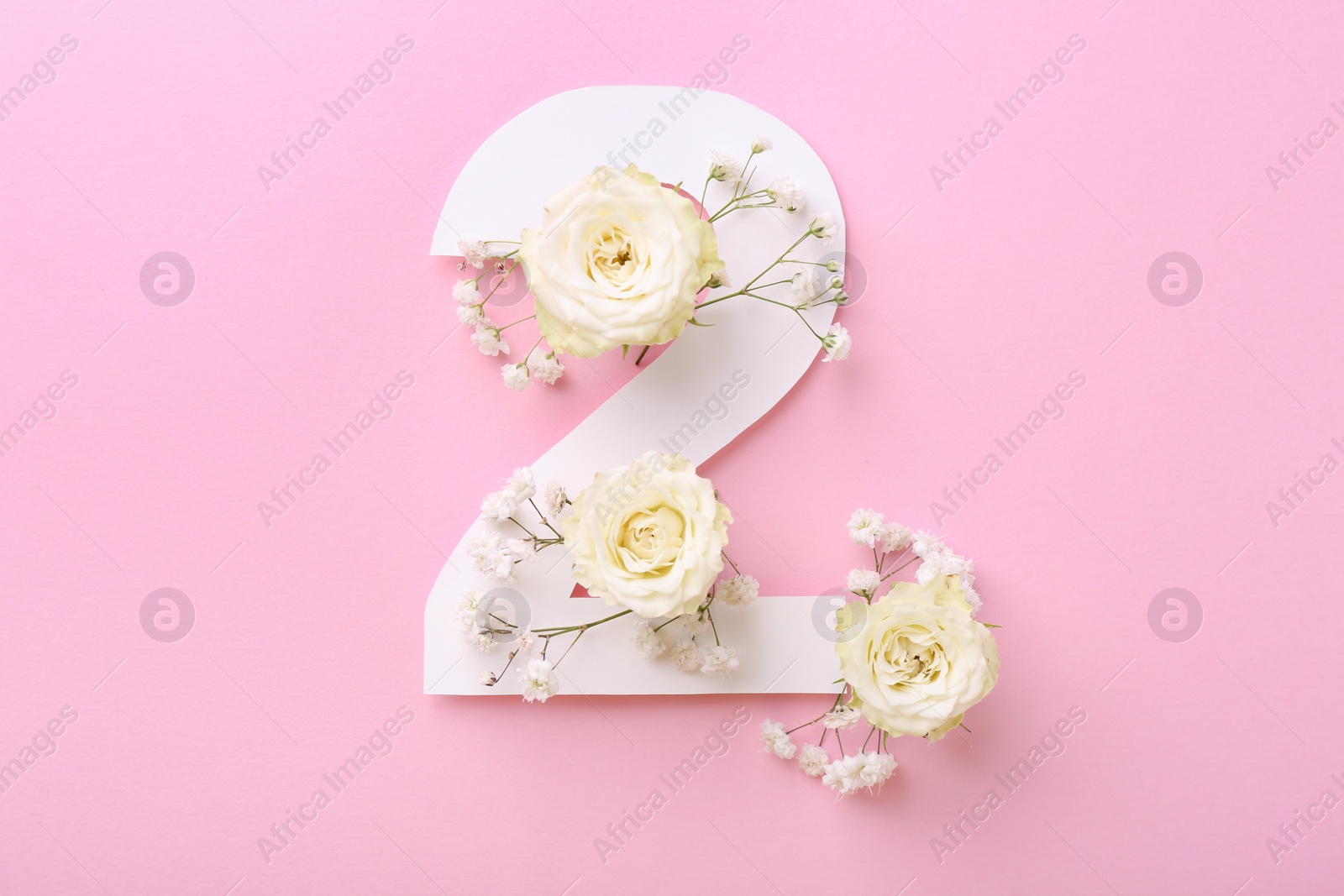 Photo of Paper number 2 and beautiful flowers on pink background, top view
