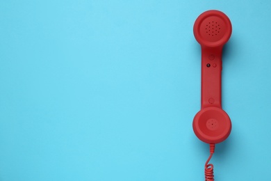 Red corded telephone handset on light blue background, top view. Hotline concept