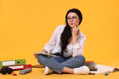 Student with notebook sitting among books and stationery on yellow background