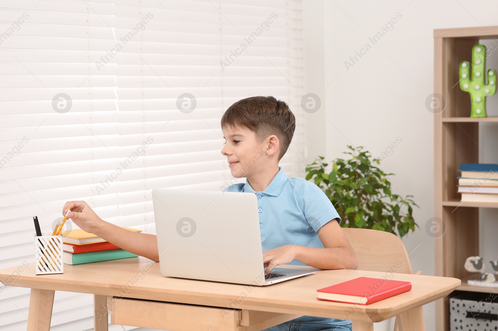 Photo of Boy using laptop at desk in room. Home workplace