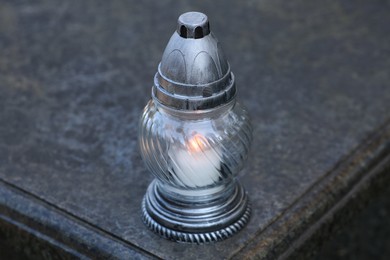 Grave lantern with burning candle on granite surface in cemetery