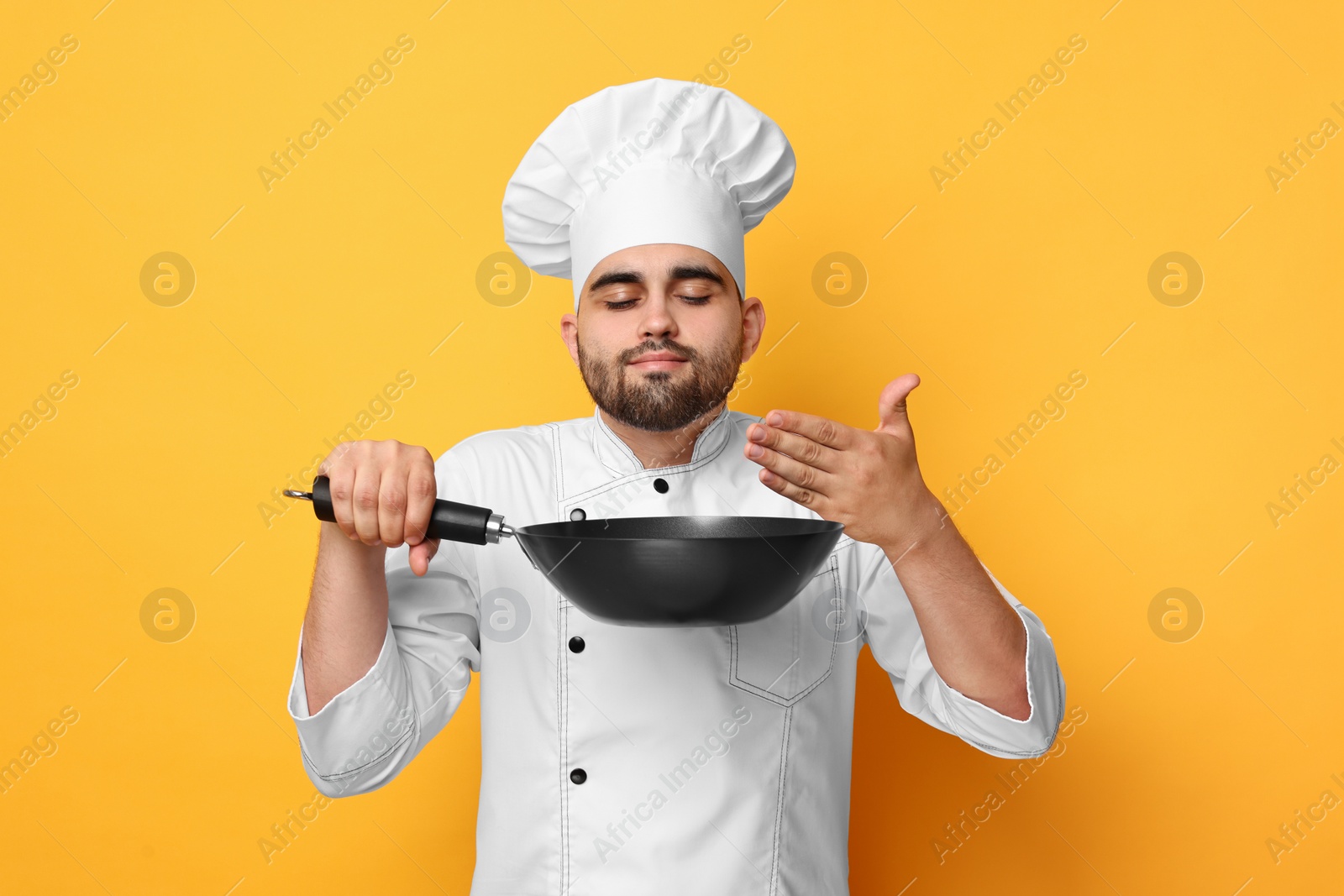 Photo of Professional chef smelling something in wok on yellow background