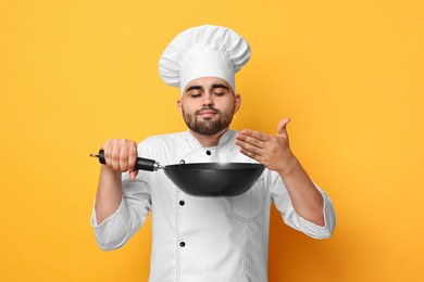 Professional chef smelling something in wok on yellow background