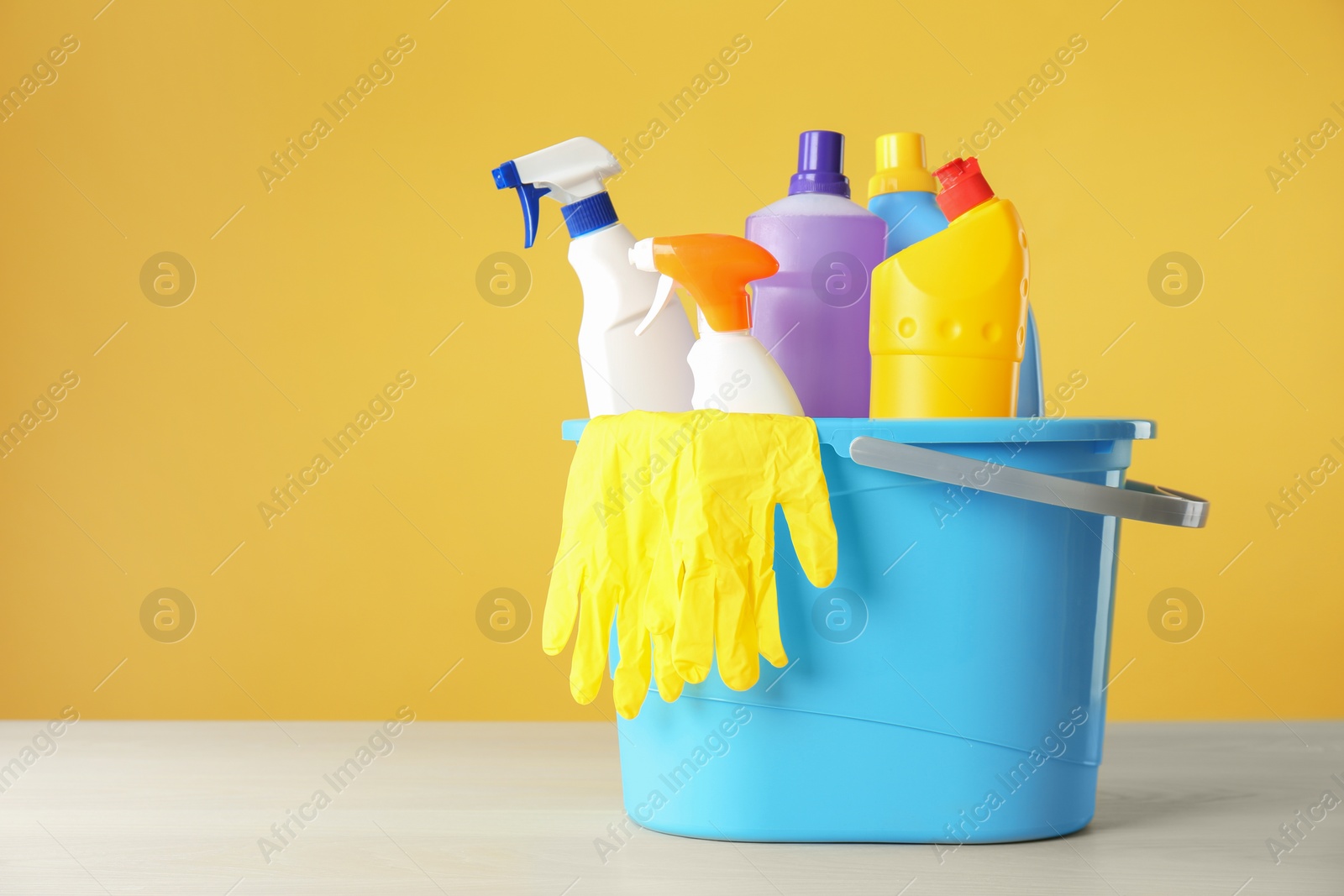 Photo of Bucket with cleaning products and gloves on grey table. Space for text