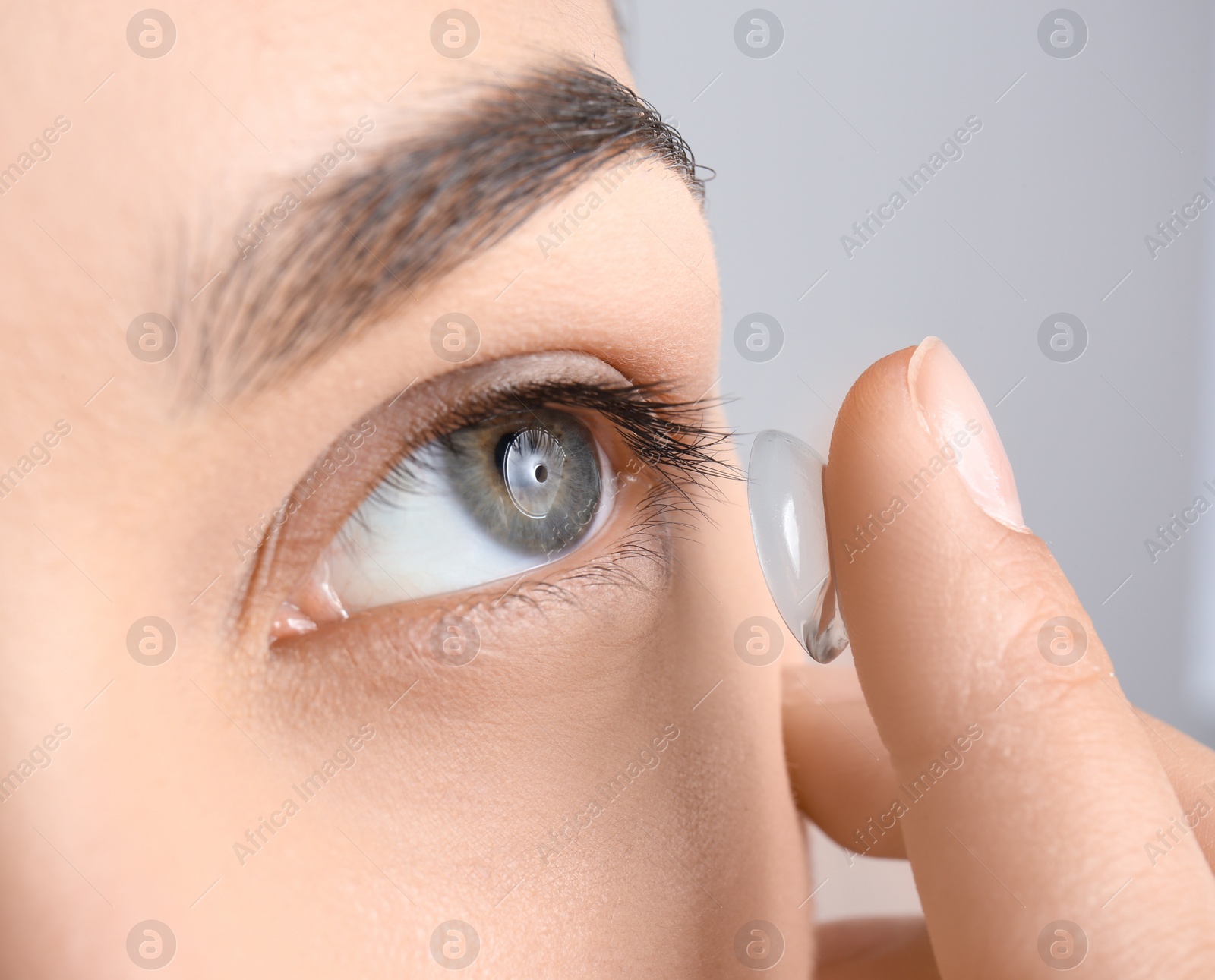 Photo of Young woman putting contact lens in her eye, closeup