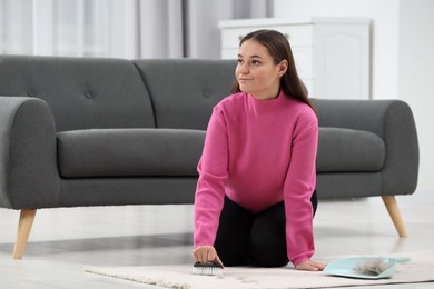 Photo of Woman with brush removing pet hair from carpet at home