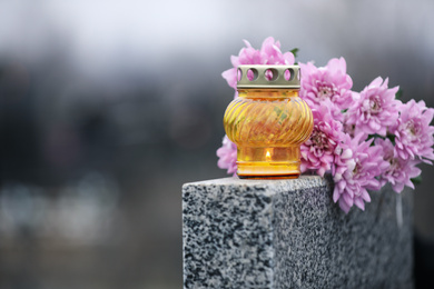 Photo of Chrysanthemum flowers and candle on grey granite tombstone outdoors. Funeral ceremony