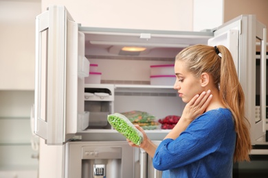 Photo of Young woman with frozen green peas near open refrigerator at home