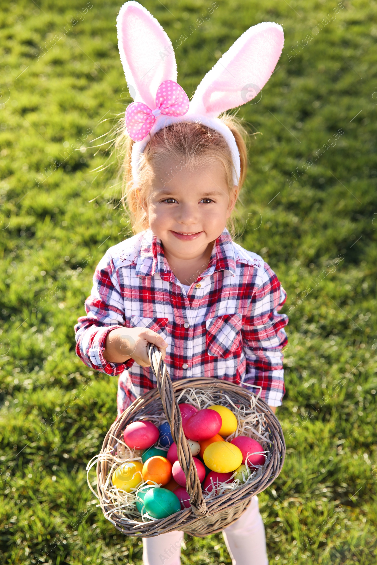 Photo of Cute little girl with bunny ears and basket of Easter eggs in park