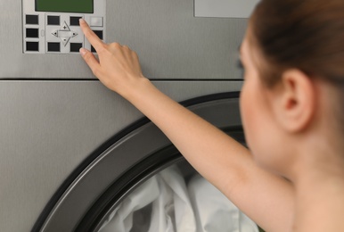 Photo of Young woman pressing buttons on washing machine in dry-cleaning