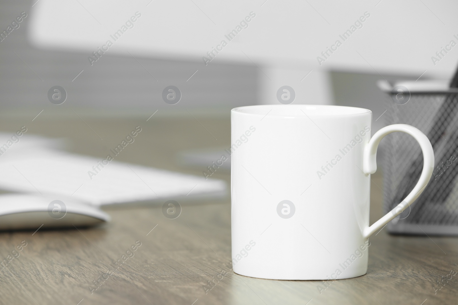 Photo of White ceramic mug on wooden table at workplace. Mockup for design