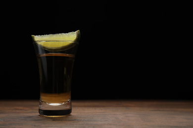 Photo of Mexican Tequila shot with lime slice on wooden table against black background. Space for text