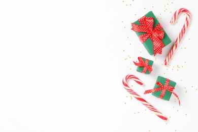 Photo of Christmas gift boxes and candy canes on white background, flat lay. Space for text