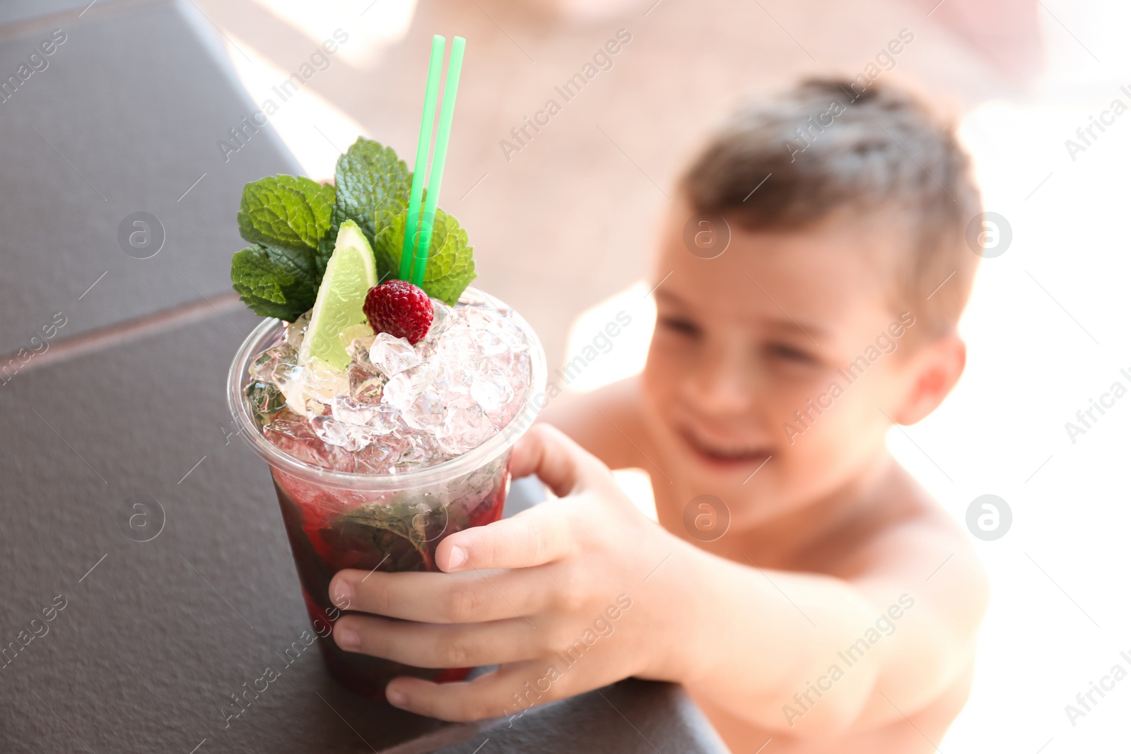 Photo of Boy with delicious refreshing drink outdoors, focus on plastic cup