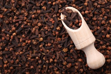 Photo of Many aromatic cloves and wooden scoop as background, top view. Space for text