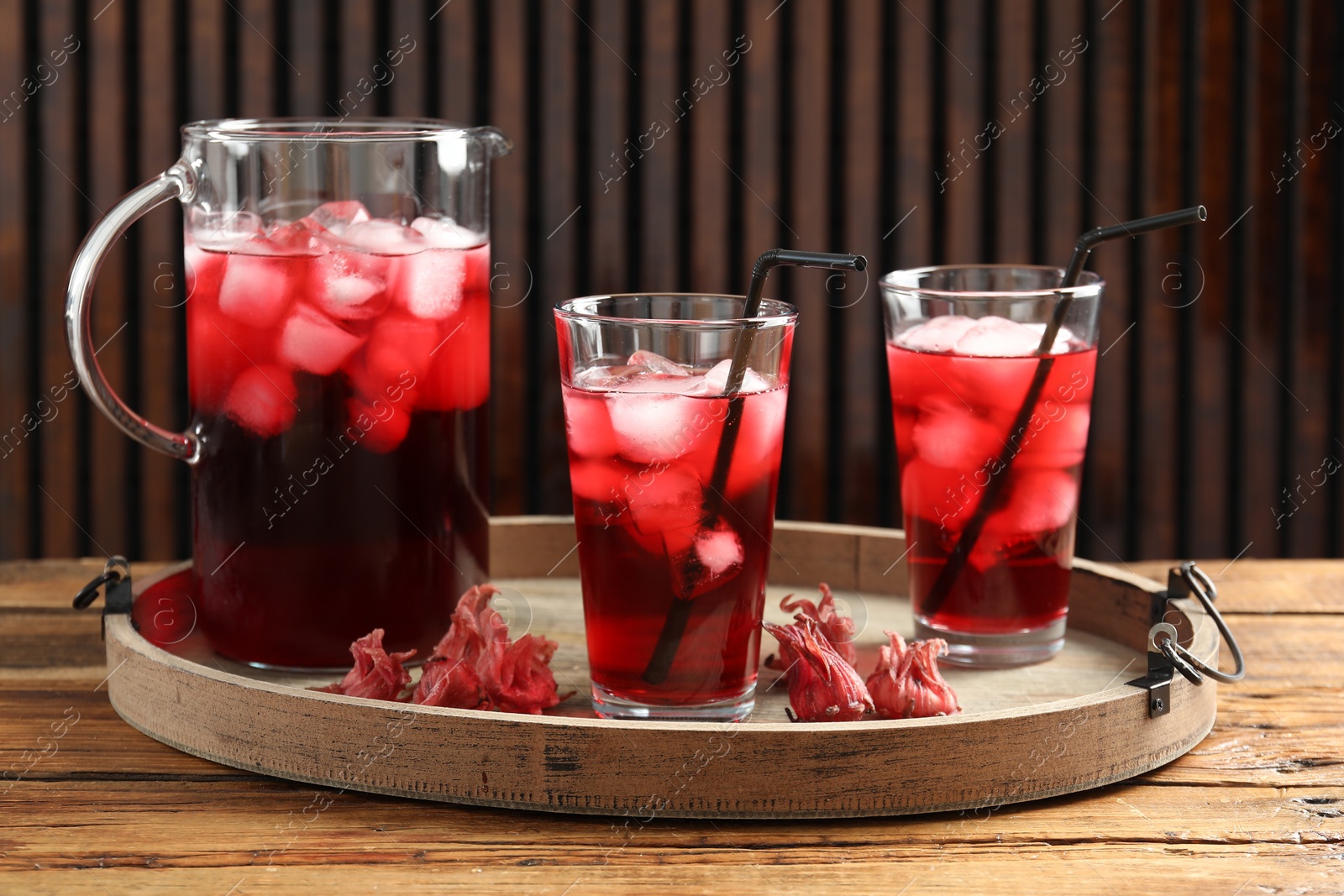 Photo of Delicious iced hibiscus tea and dry flowers on wooden table
