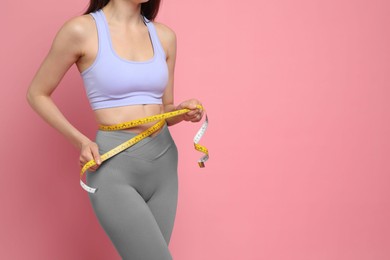 Photo of Woman with measuring tape showing her slim body on pink background, closeup. Space for text