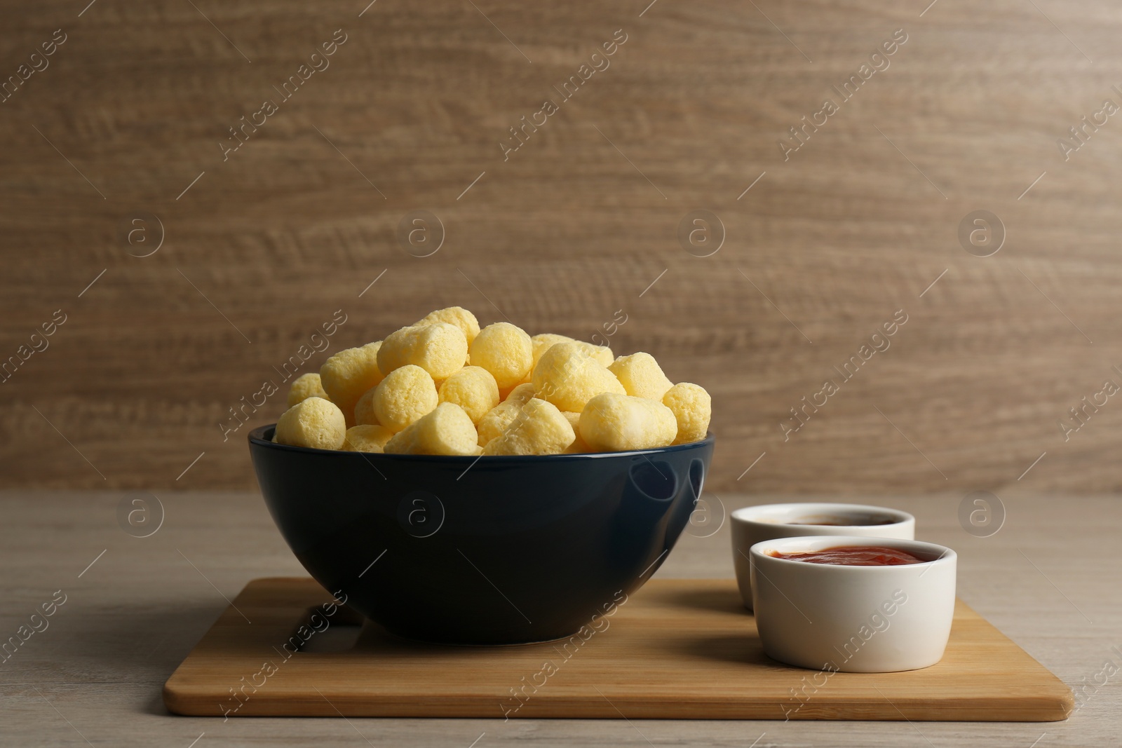 Photo of Bowl of corn sticks served with sauces on wooden table, space for text