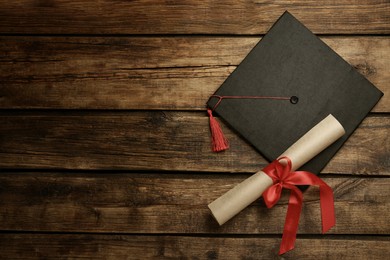 Image of Graduation hat and diploma on wooden table, flat lay. Space for text