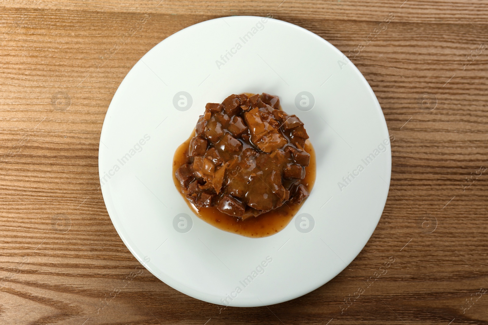 Photo of Plate with wet pet food on wooden table, top view