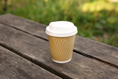 Photo of Paper cup on wooden bench outdoors. Coffee to go