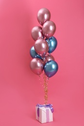 Bright balloons and gift box on color background