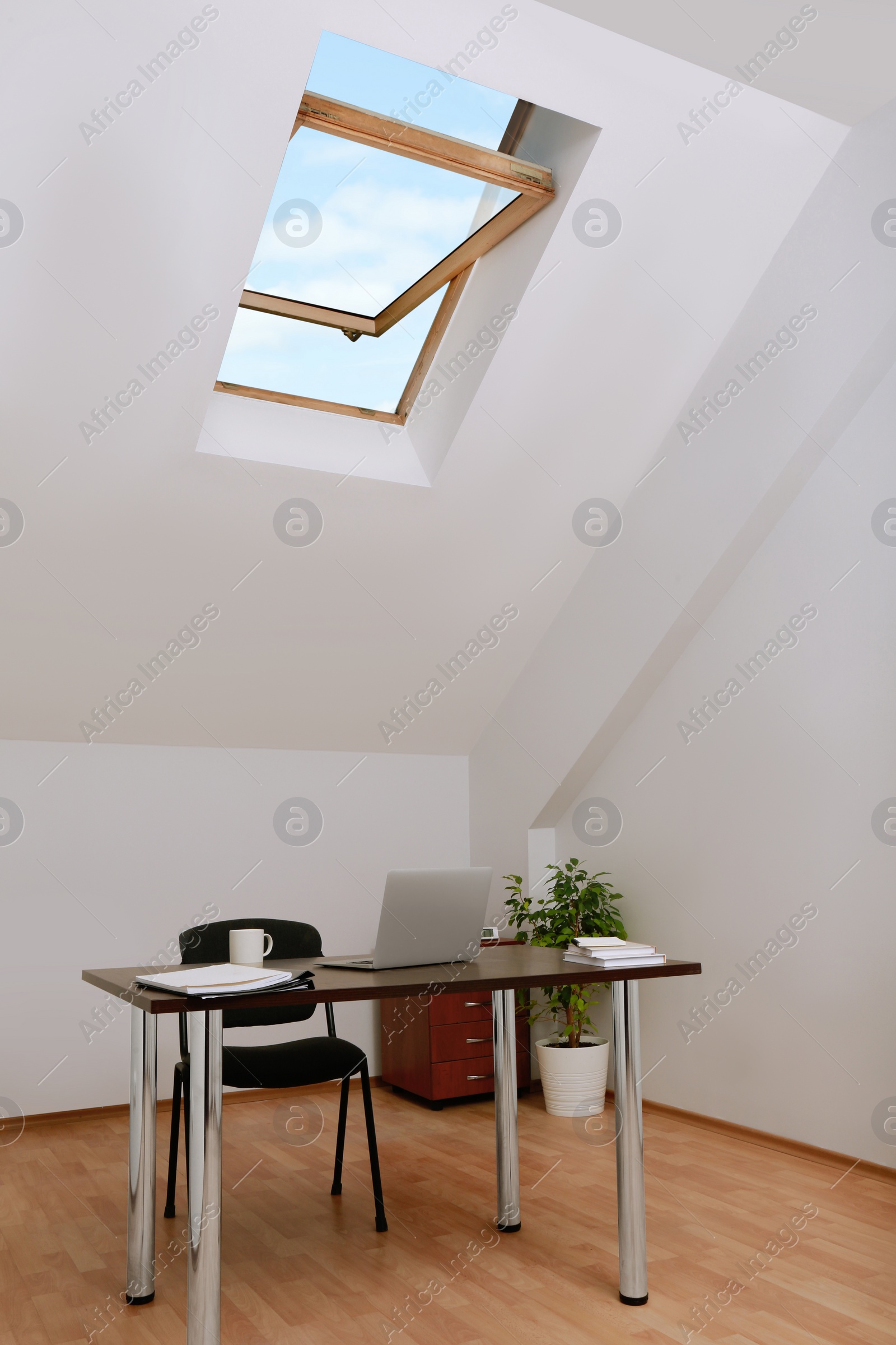 Photo of Stylish workplace with laptop and documents in attic room. Interior design