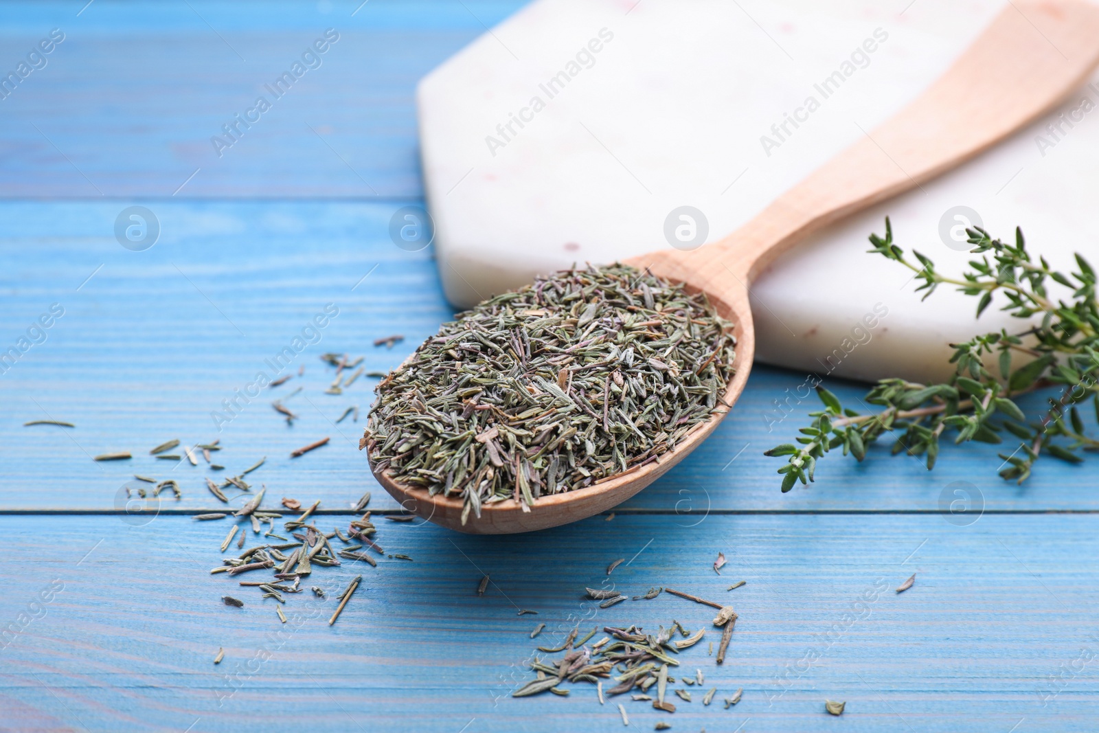 Photo of Spoon with dried thyme on light blue wooden table