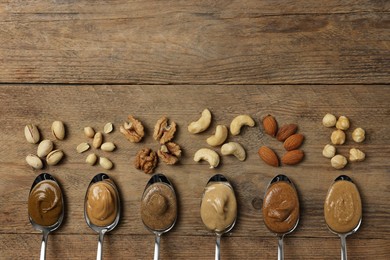 Photo of Tasty nut butters in spoons and raw nuts on wooden table, flat lay. Space for text