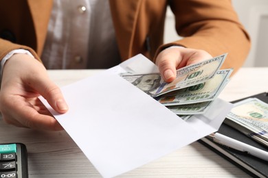 Money exchange. Woman putting dollar banknotes into envelope at white wooden table, closeup