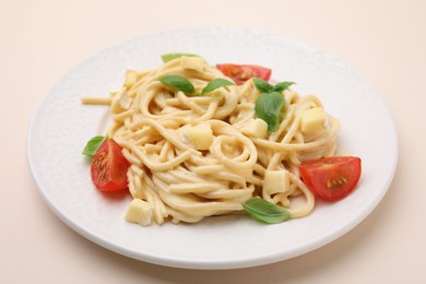 Photo of Delicious pasta with brie cheese, tomatoes and basil leaves on beige table, closeup