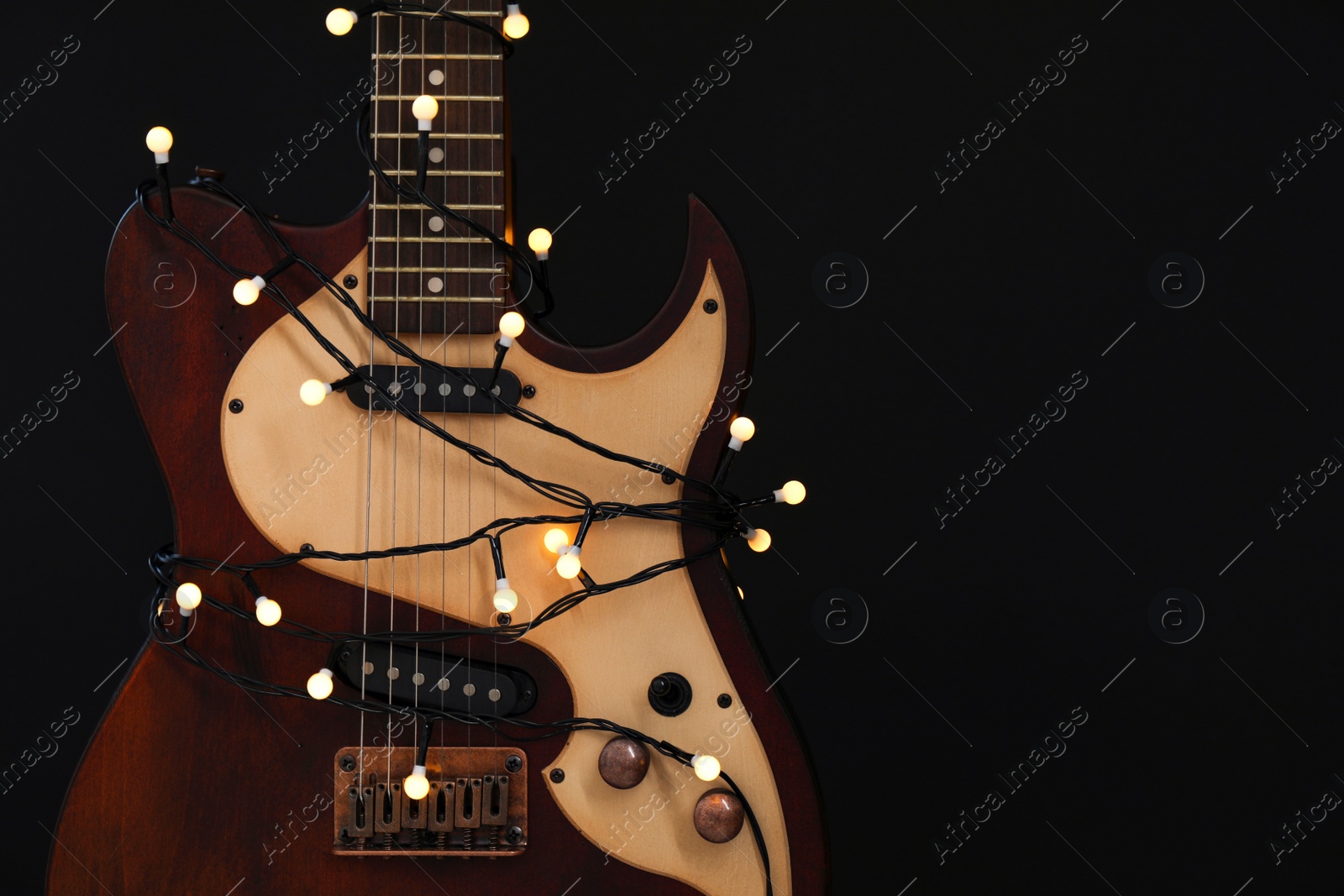 Photo of Guitar with golden lights on black background, space for text. Christmas music