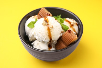 Tasty ice cream with caramel sauce, mint, candies and nuts in bowl on yellow background, closeup