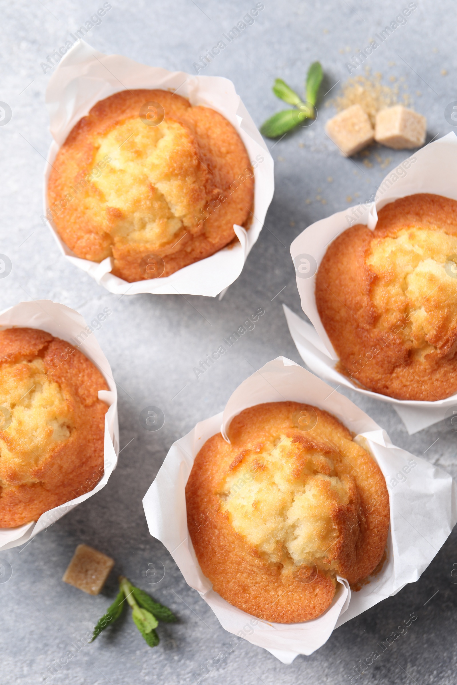 Photo of Delicious sweet muffins and brown sugar on light grey textured table, flat lay