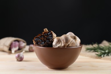 Photo of Bulbs of fermented black garlic in bowl on wooden table