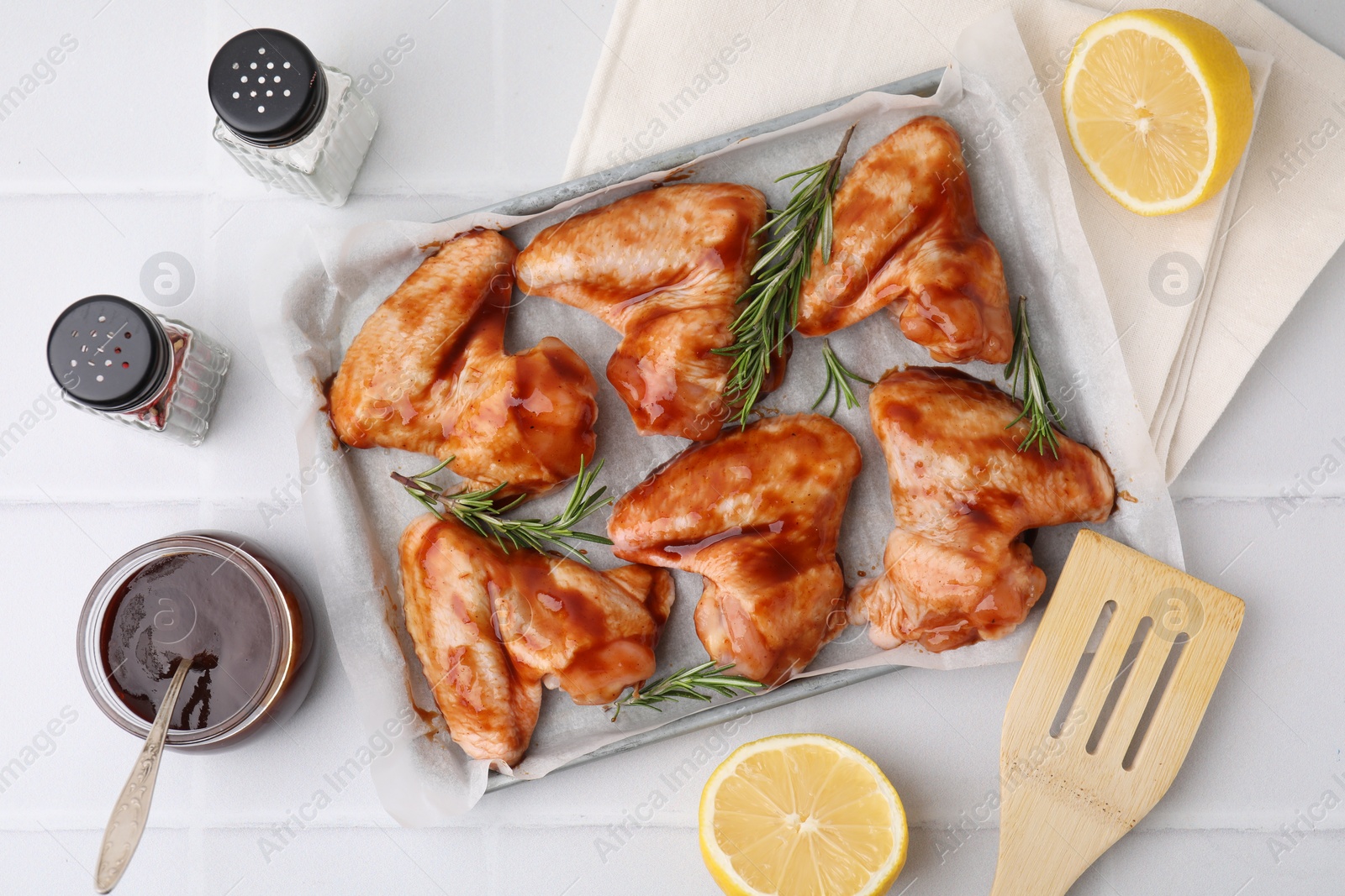 Photo of Raw chicken wings, rosemary, marinade and spices on light tiled table, flat lay