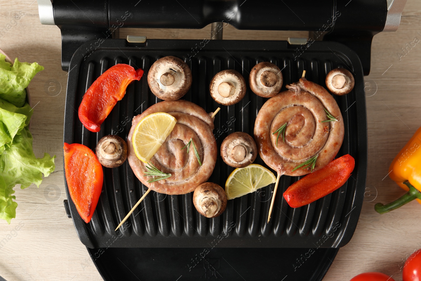 Photo of Electric grill with homemade sausages and vegetables on wooden table, flat lay