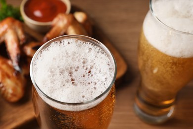 Glasses with beer and delicious baked chicken wings on wooden table, closeup