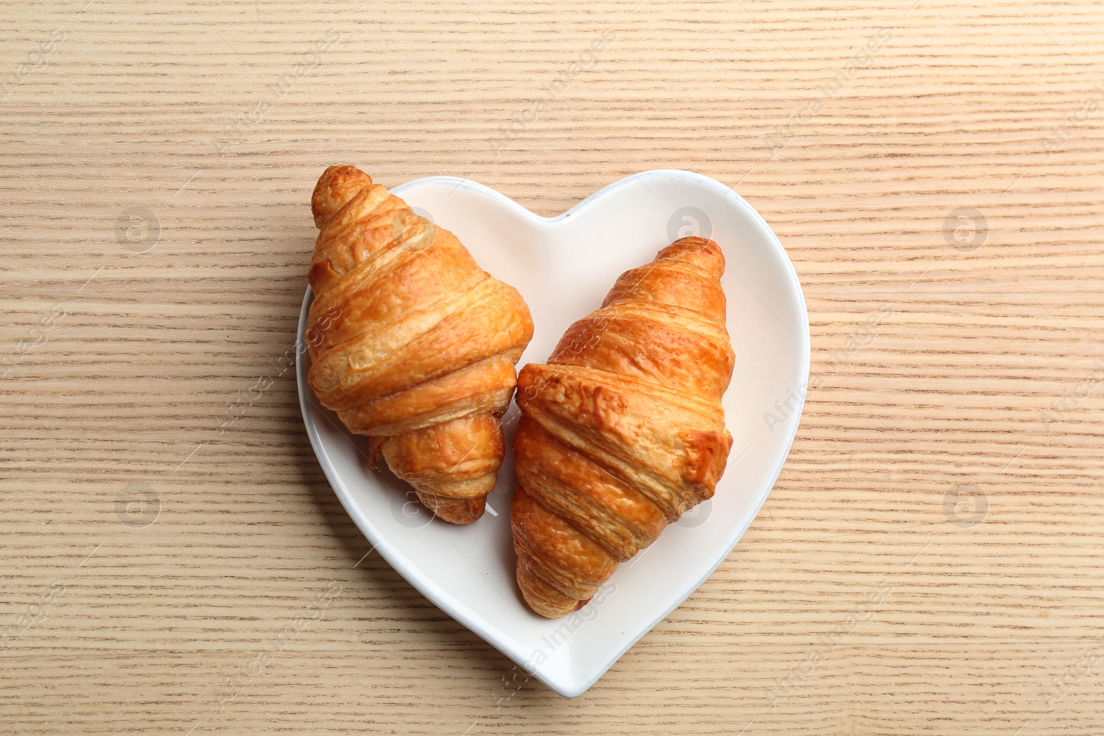 Photo of Plate of fresh croissants on wooden background, top view. French pastry