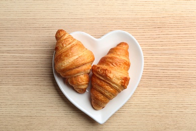 Plate of fresh croissants on wooden background, top view. French pastry