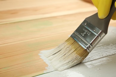 Worker applying white paint onto wooden surface, closeup. Space for text